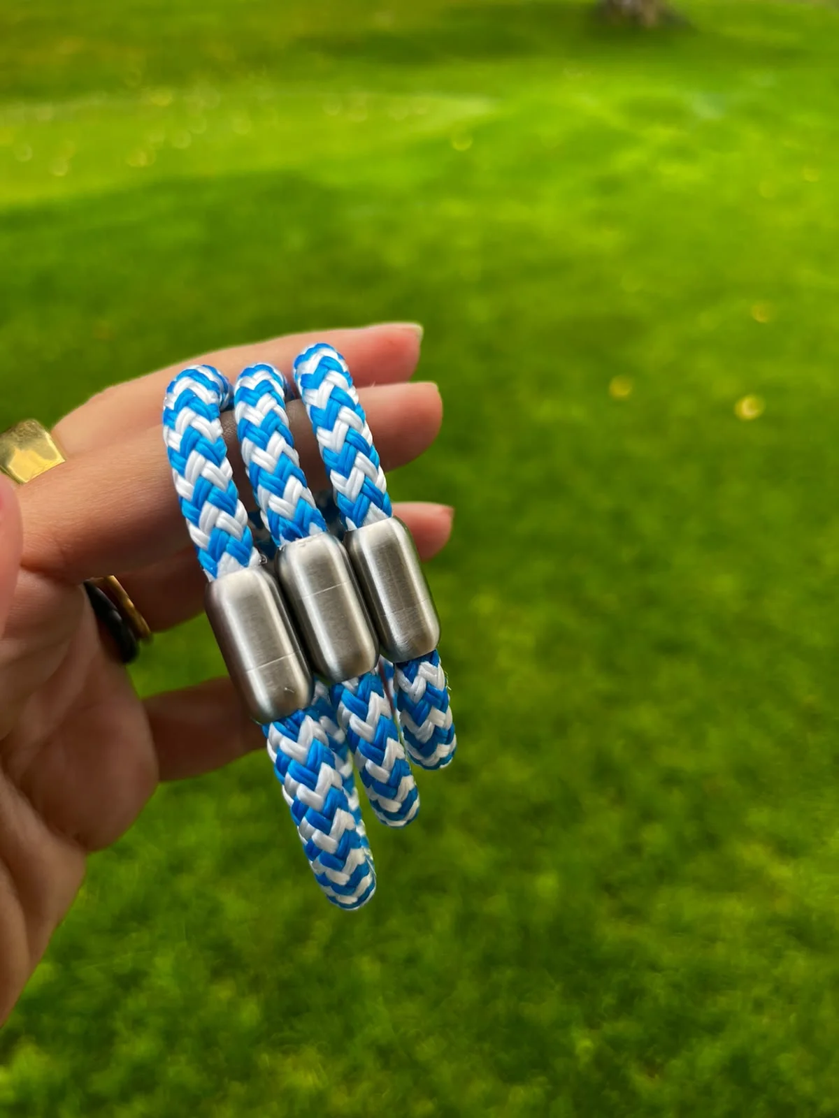Three handmade Himmelblau bracelets in blue and white with stainless-steel clasps, held in a hand