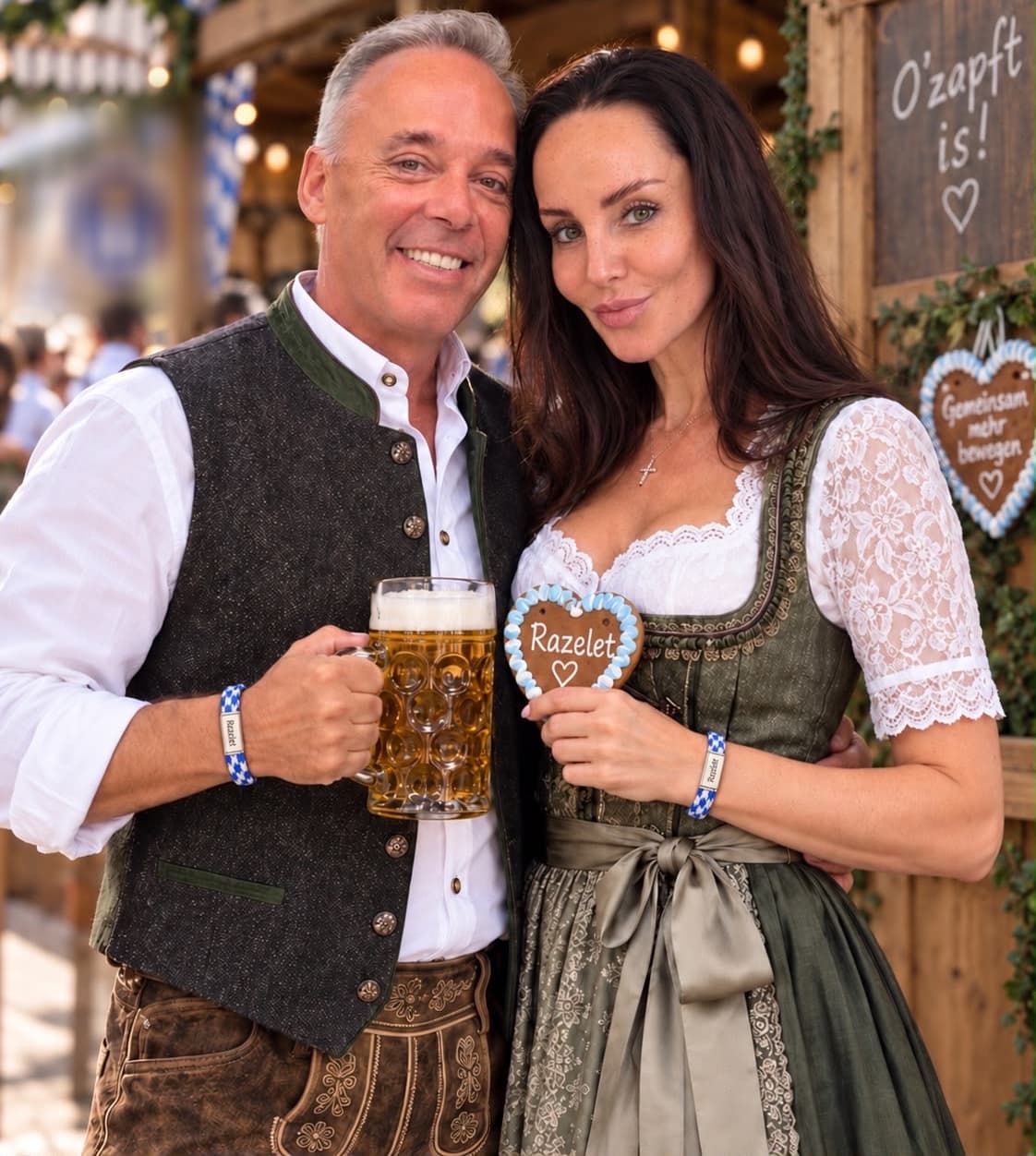 Ein Paar in Tracht auf der Wiesn, beide tragen das blau-weiße Razelet-Band, sie hält ein Lebkuchenherz mit der Aufschrift Razelet